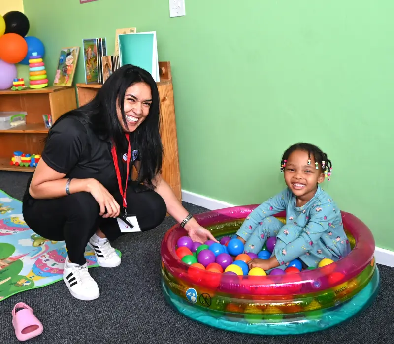 lady next to child sitting an a small pool of balls